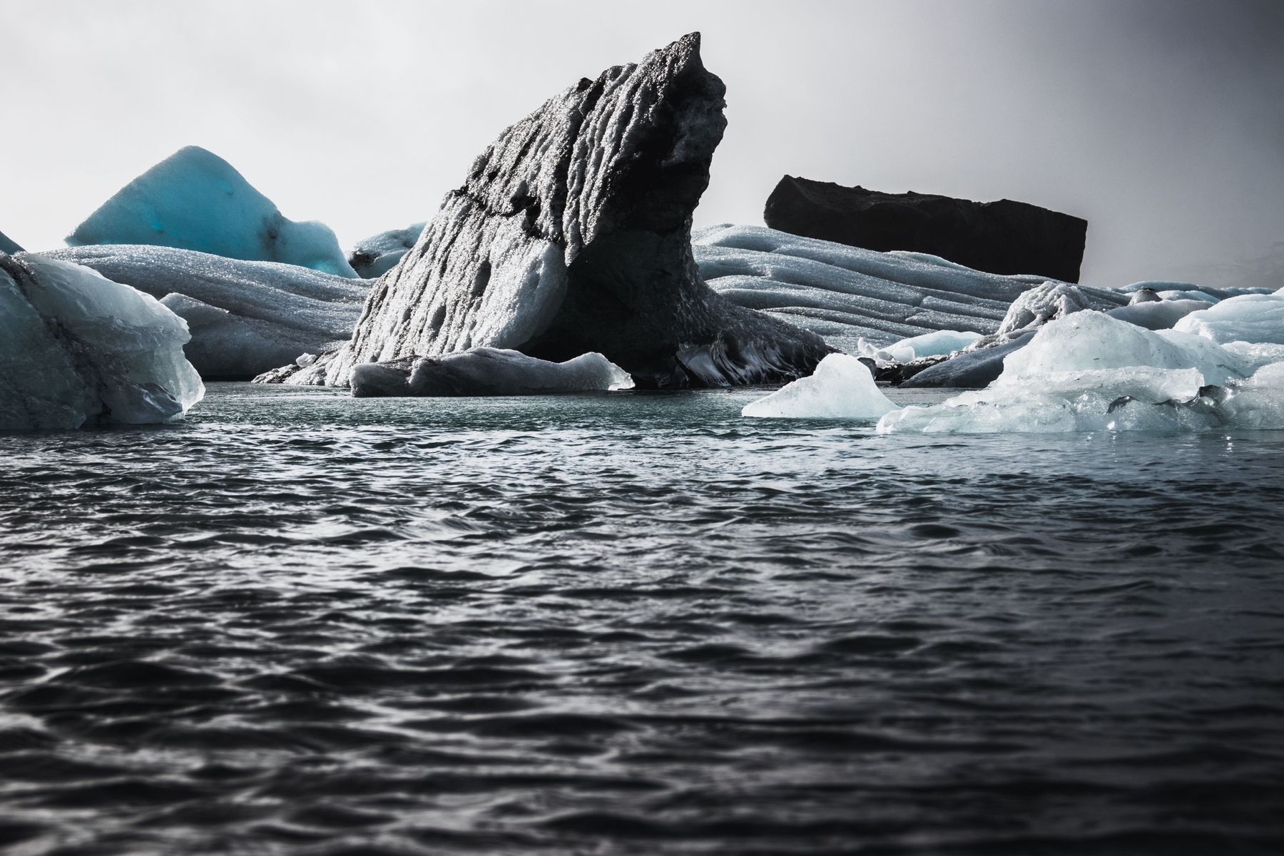 A dark, ash-streaked iceberg rising from choppy grey water