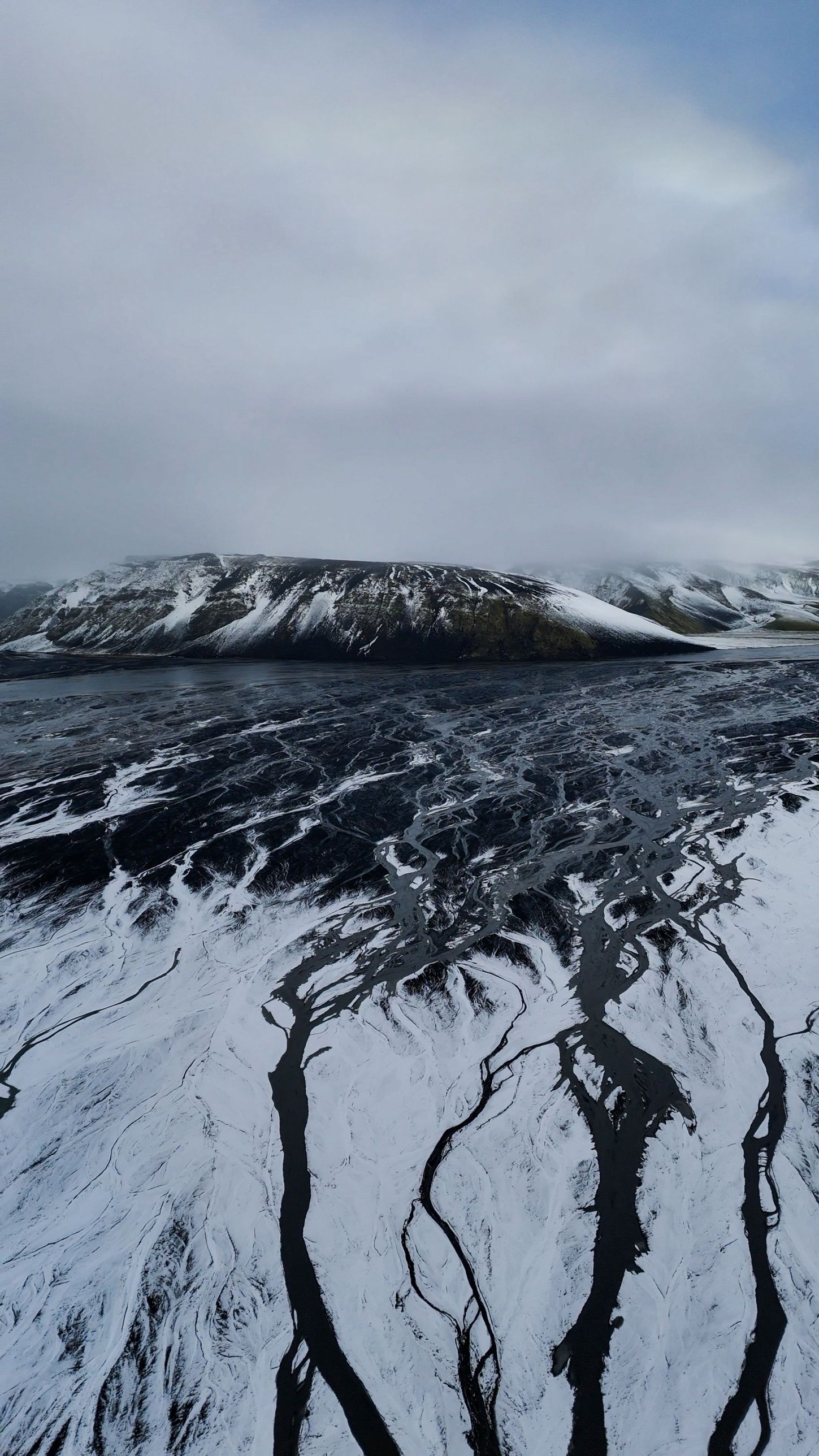 Black meltwater channels branching across a snow-covered plain