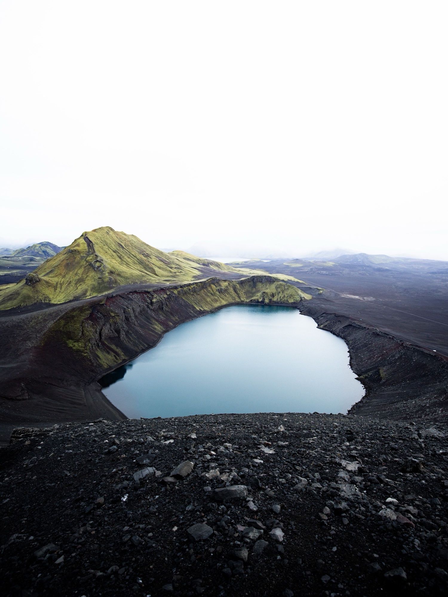 A blue crater lake beside a moss-green mountain