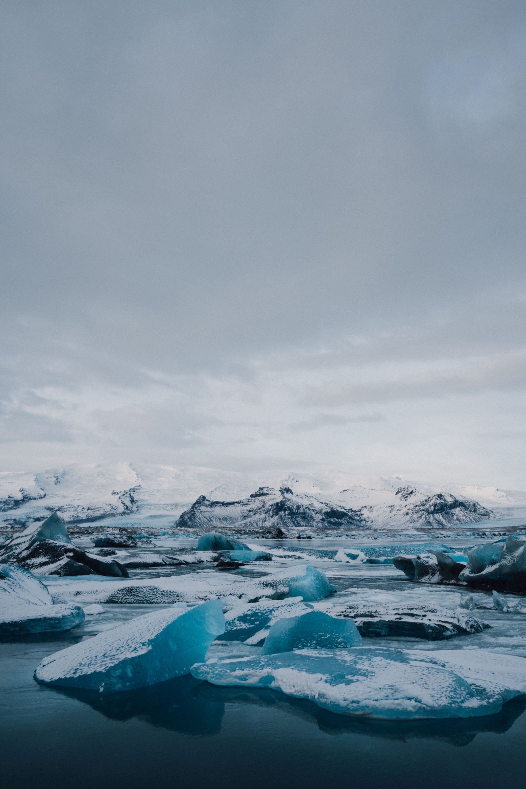 Snow-dusted blue icebergs in Jökulsárlón below white mountains