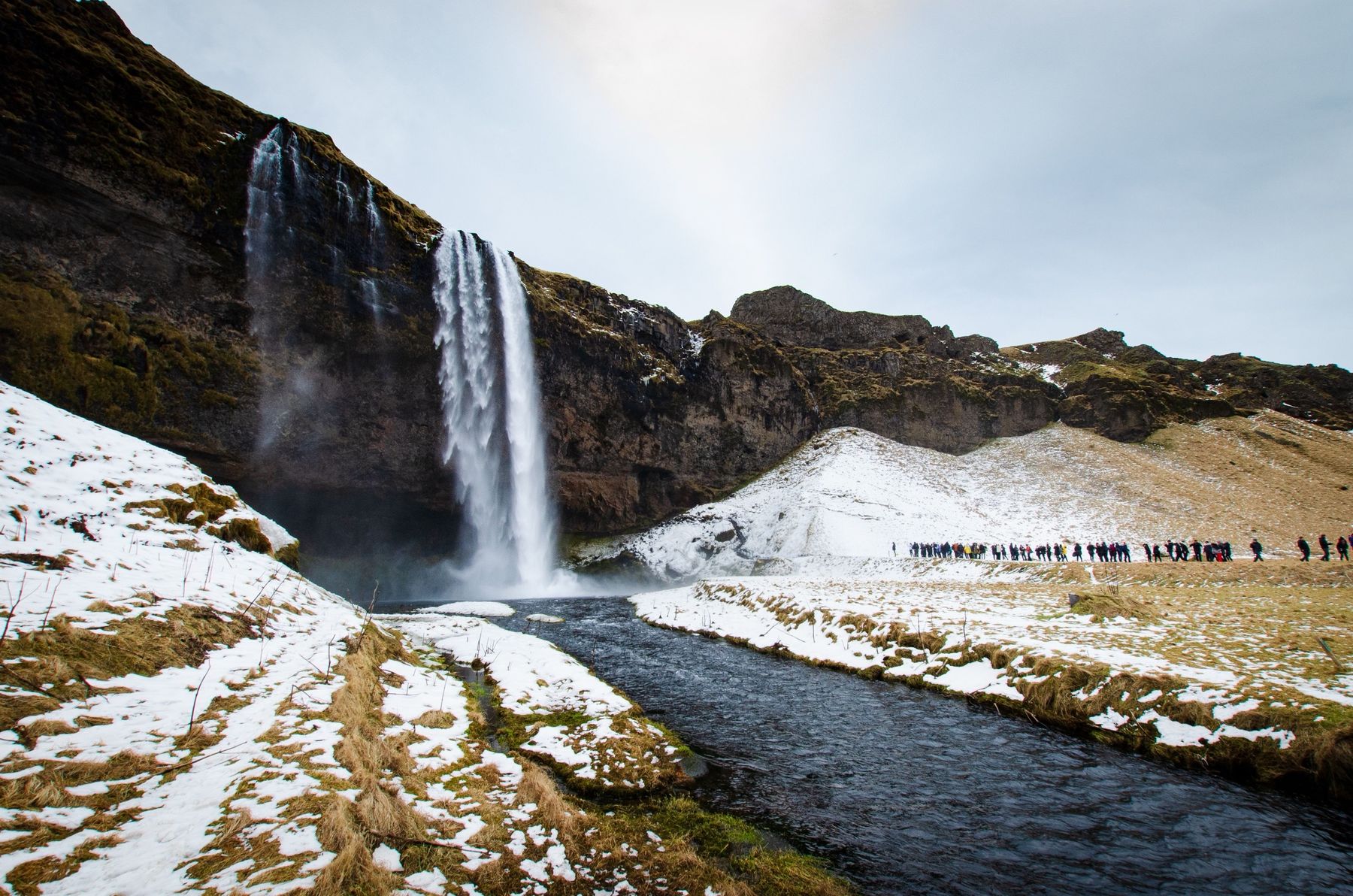 Seljalandsfoss in winter with snow on the slopes and walkers on the path