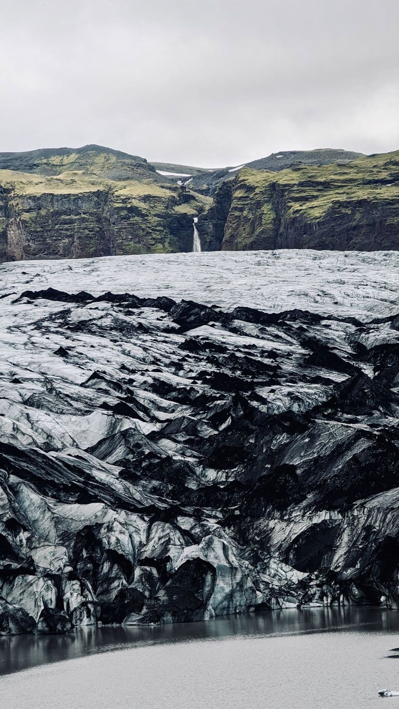 The ash-streaked ice of Sólheimajökull with a waterfall in the cliffs above