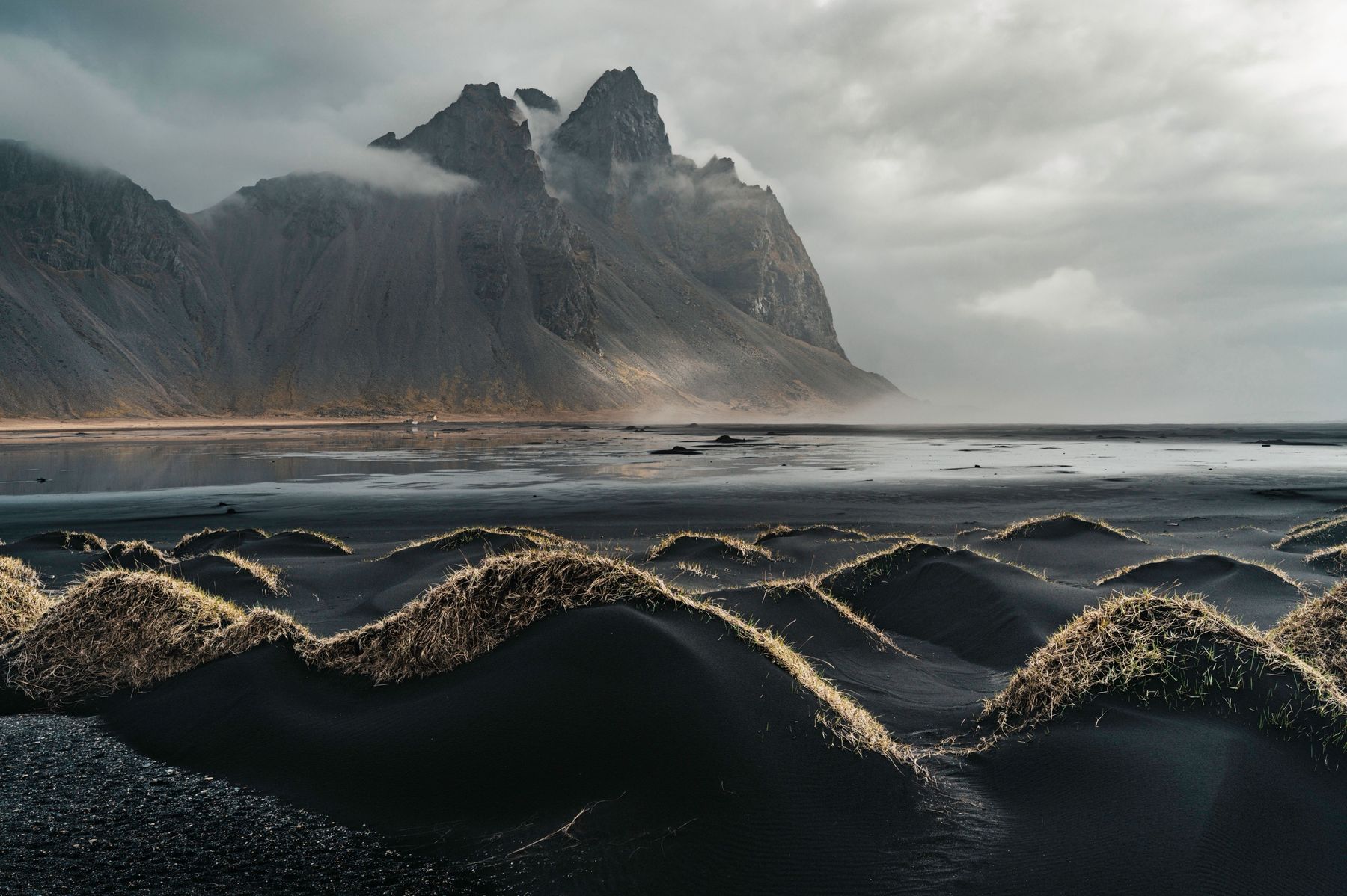 Grass-topped black dunes in front of Vestrahorn wrapped in mist